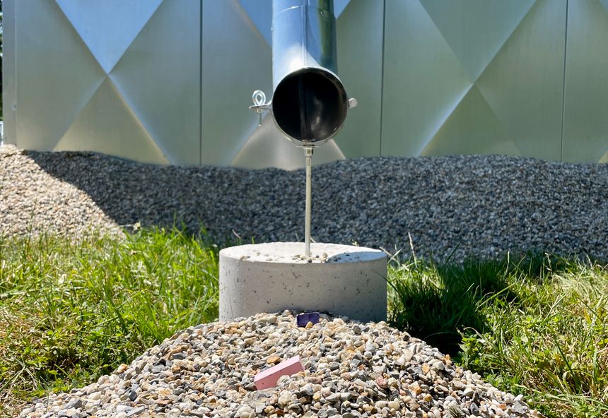 Steel well casing pipe capped over a concrete pad on a rural lot